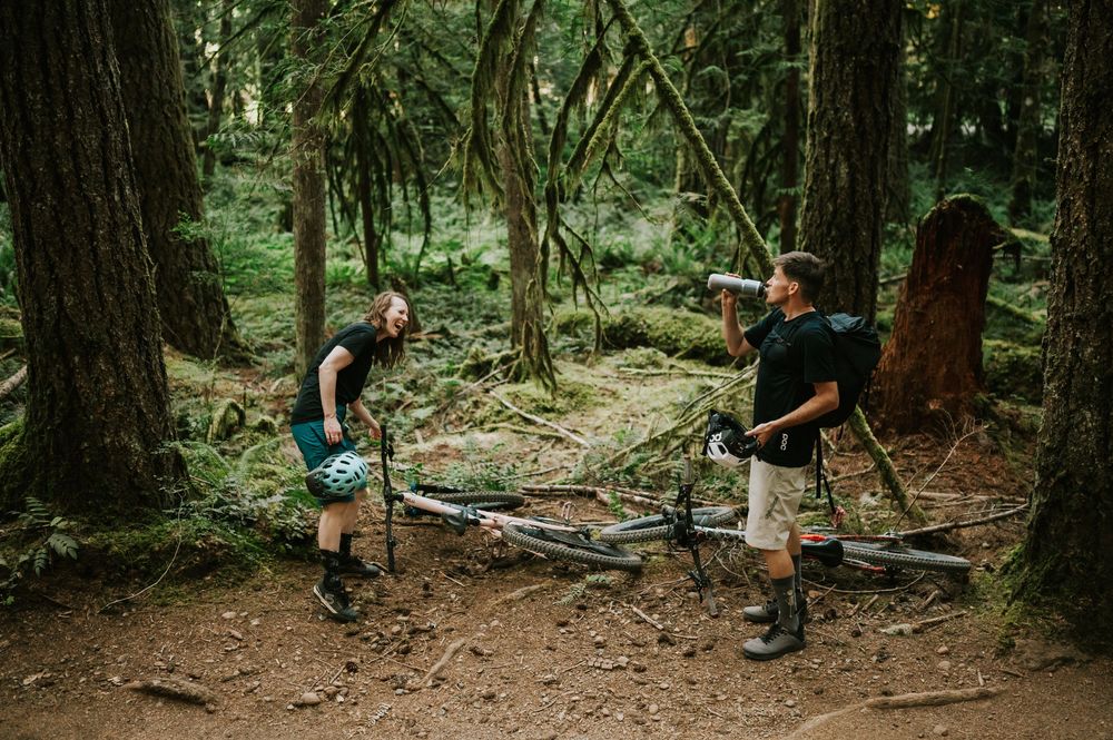 Adventurous couple engagement session photo of couple drinking biking water bottles in Cumberland Forest Vancouver Island