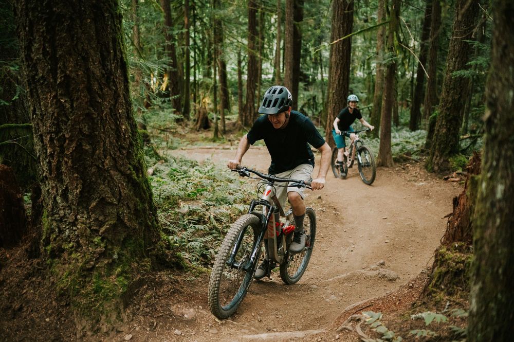 Adventurous couple engagement session photo of couple biking up trail in Cumberland Forest Vancouver Island through trees