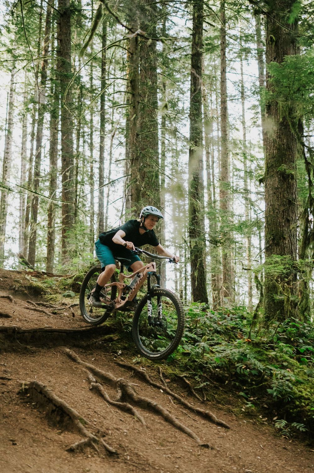Adventurous couple engagement session photo of couple biking down trail hill in Cumberland Forest Vancouver Island doing jump