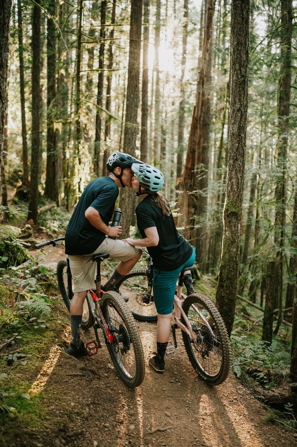 Adventurous couple engagement session photo of couple on bikes kissing in sunset light in Cumberland Forest Vancouver Island