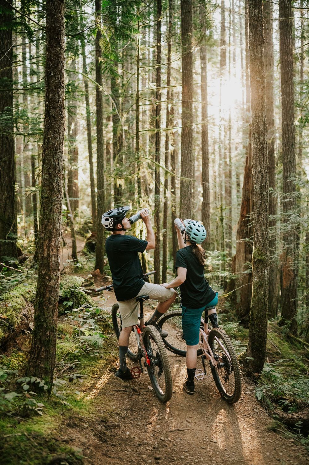 Adventurous couple engagement session photo of couple on bikes drinking water in sunset light in Cumberland Forest Vancouver Island