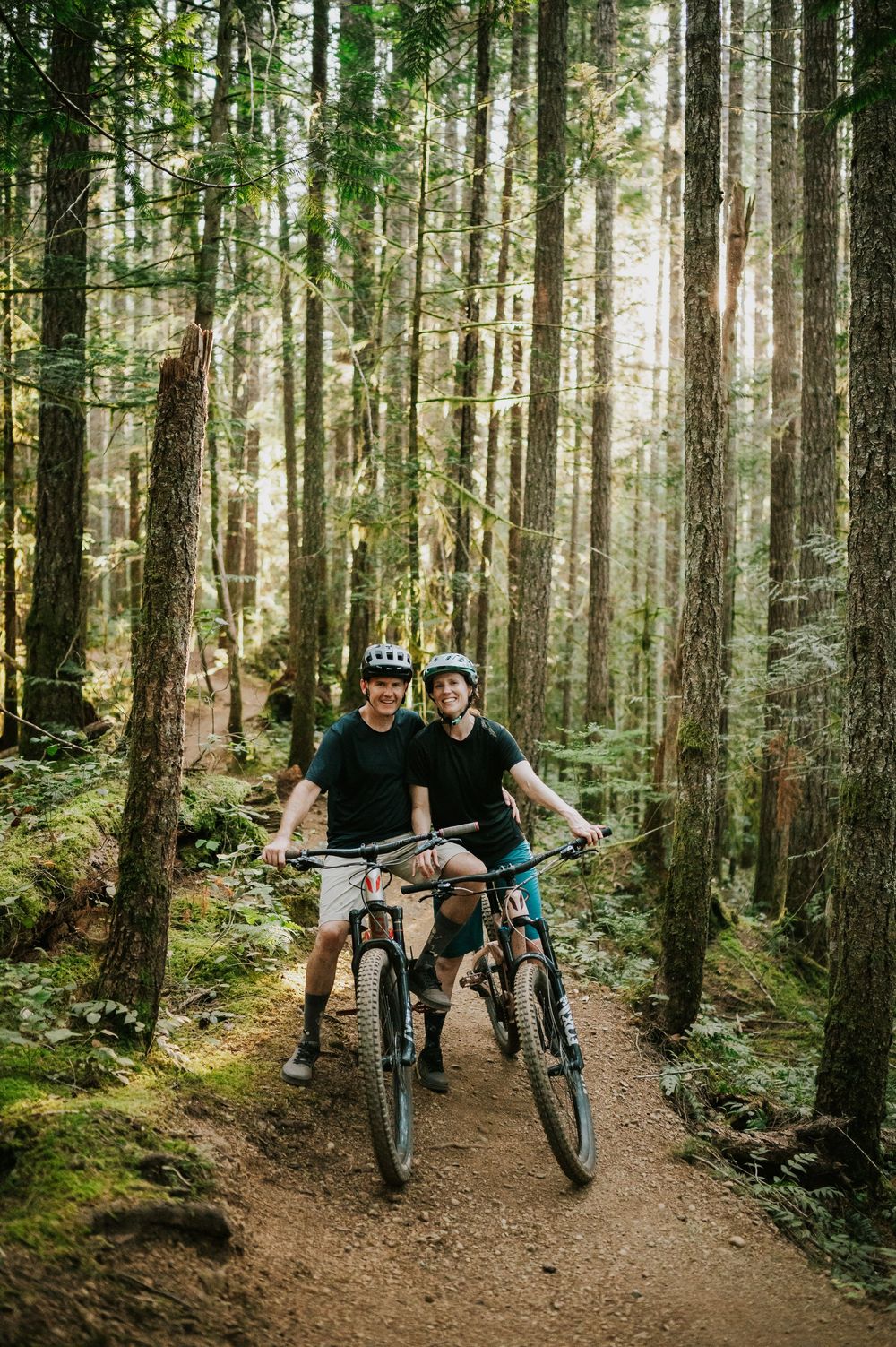 Adventurous couple engagement session photo of couple on bikes smiling in sunset light in Cumberland Forest Vancouver Island