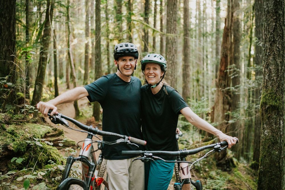Adventurous couple engagement session photo of couple on bikes smiling in sunset light in Cumberland Forest Vancouver Island