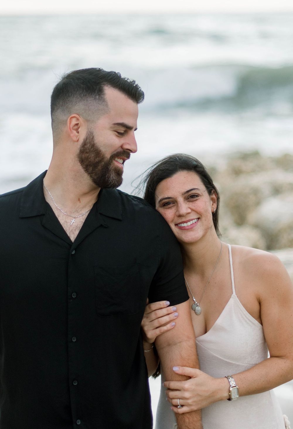 A romantic couple shares intimate moments and laughter during a beachside photo session.