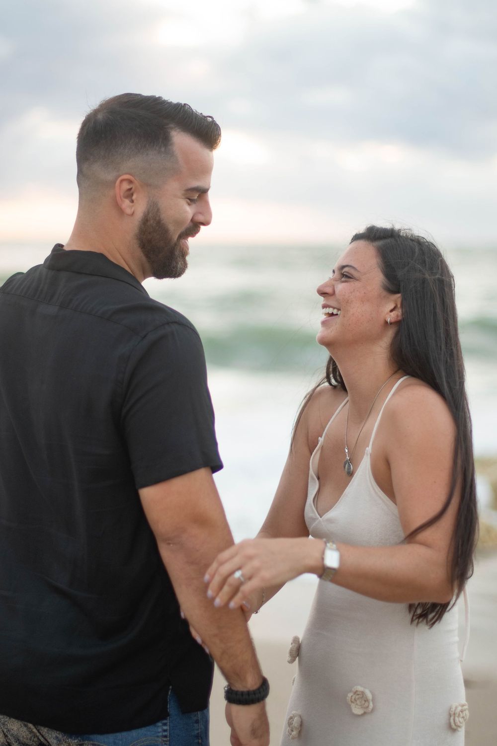 A couple shares joyful laughter during their beach photoshoot at sunset.
