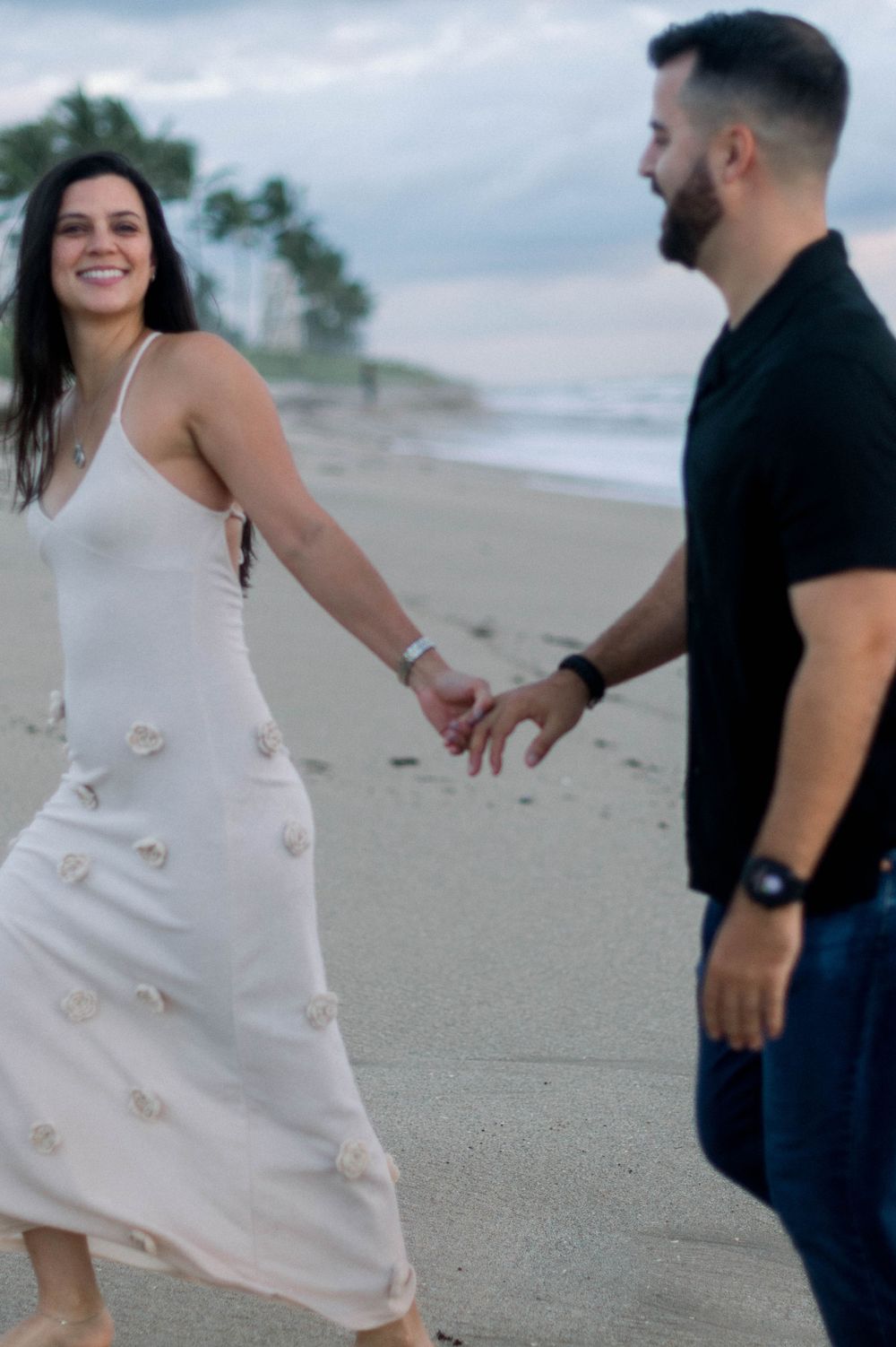 A couple shares a joyful moment together on a sandy beach, with the bride wearing a white dress.