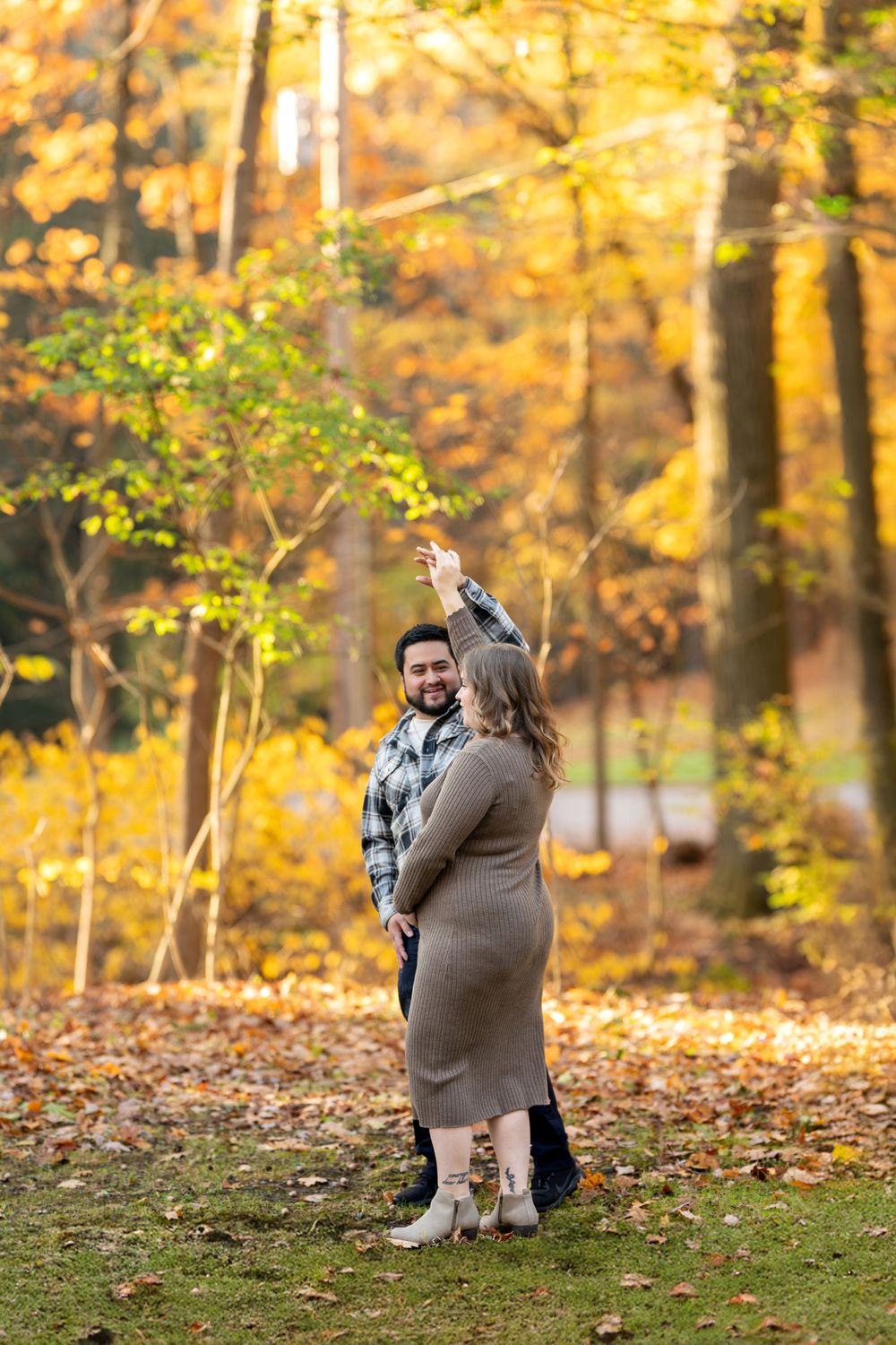 Man spinning pregnant partner in a playful dance among vibrant fall foliage in the forest.