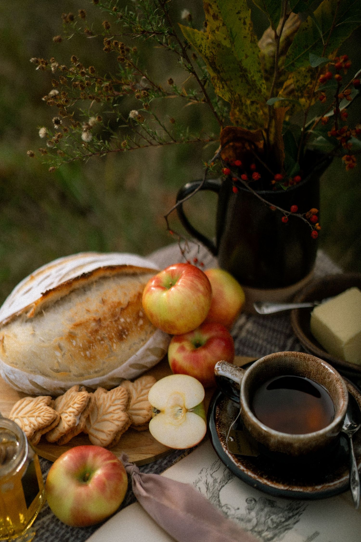 Rustic still life with fresh apples, bread loaf and hot beverage in vintage setting with moody lighting.