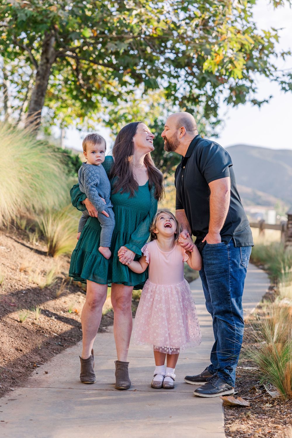 A family shares joyful moments together during an outdoor photo session on a path surrounded by greenery.