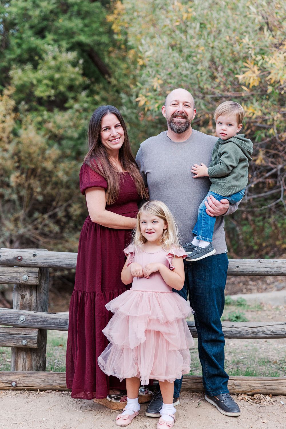 A family poses together outdoors on a wooden fence during an autumn photo session.