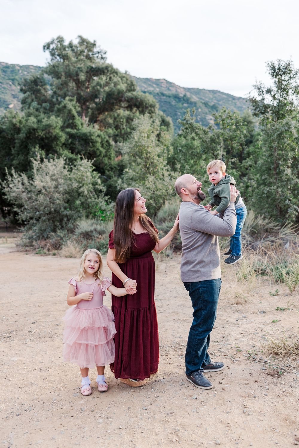 A family shares a playful moment together outdoors with mountains and trees in the background.