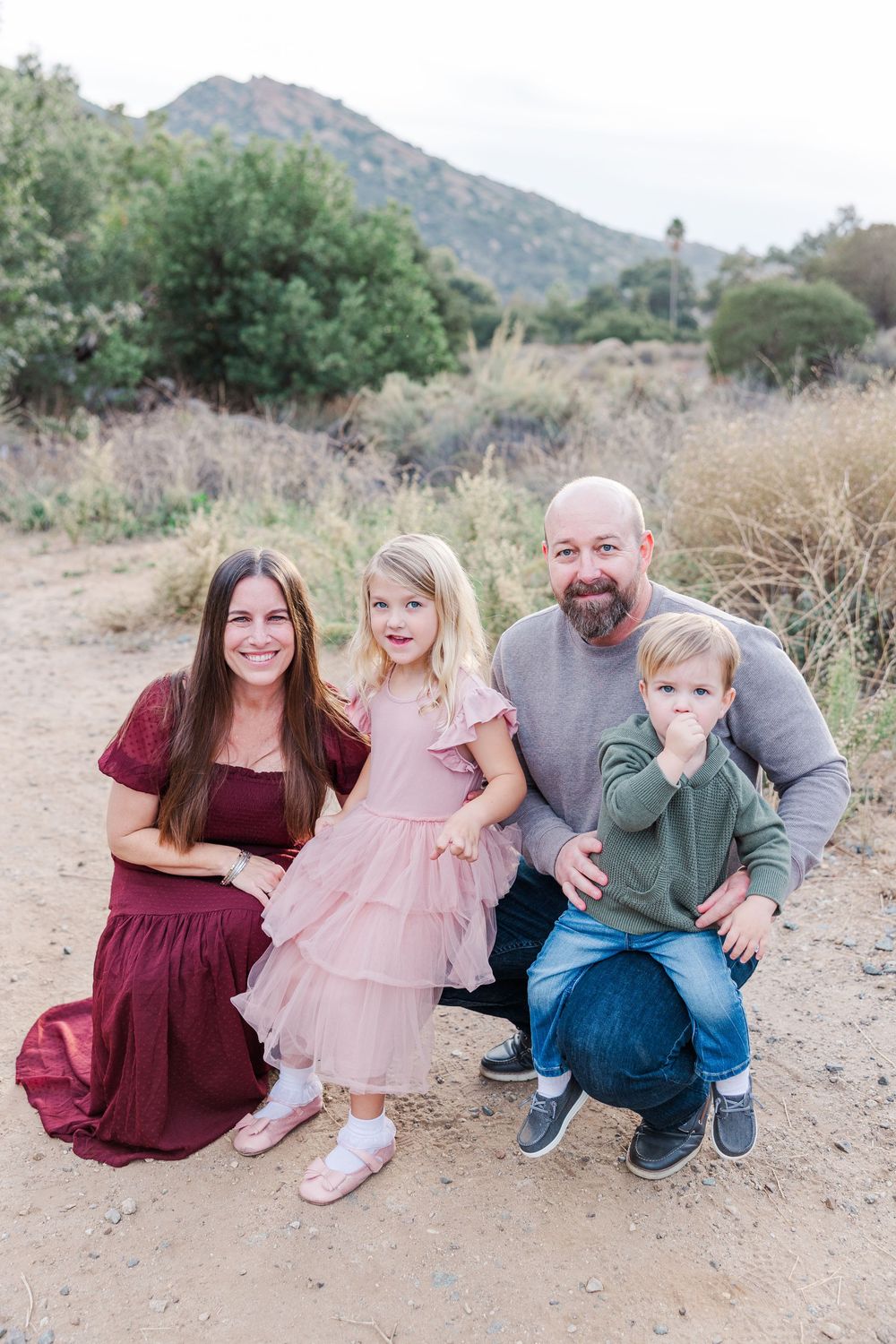 Family sitting together on a dirt trail with mountains and greenery in the background.