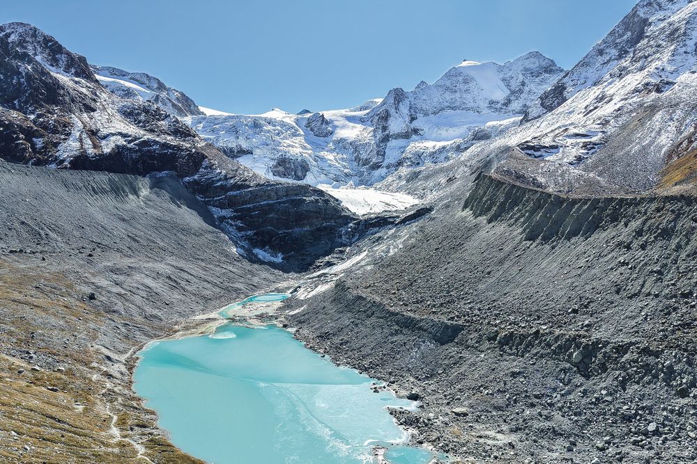 Panoramic view of snow-capped mountains surrounding a turquoise glacial lake in a rugged alpine landscape.