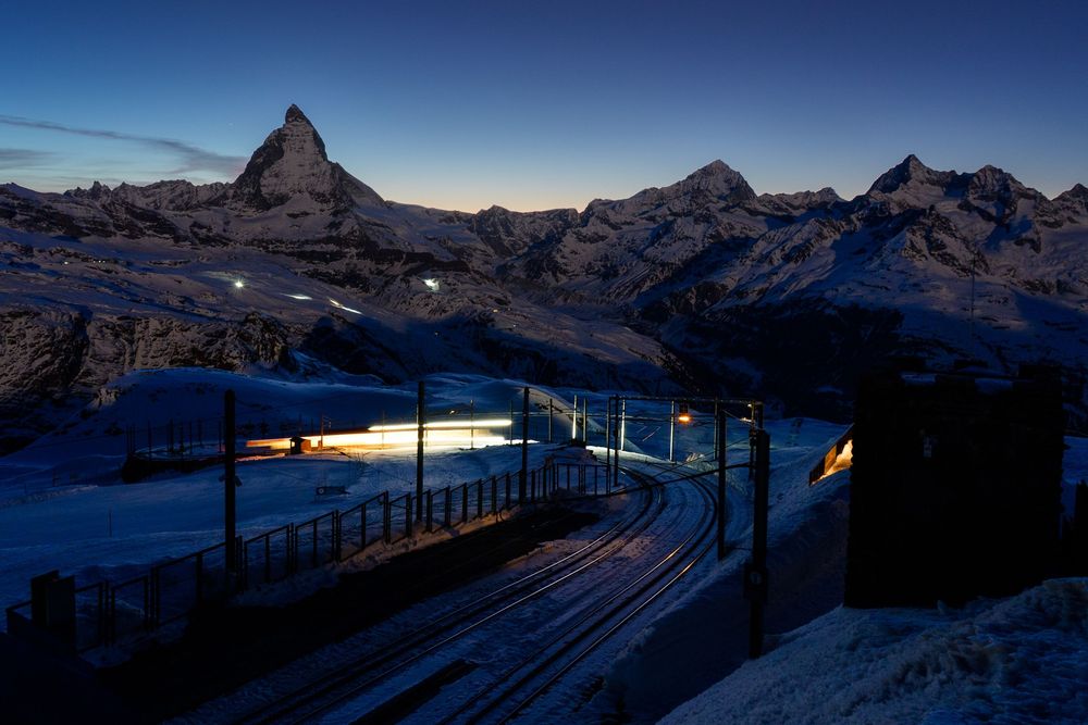 Snow-covered Matterhorn mountain at dusk with illuminated train tracks in Zermatt, Switzerland.