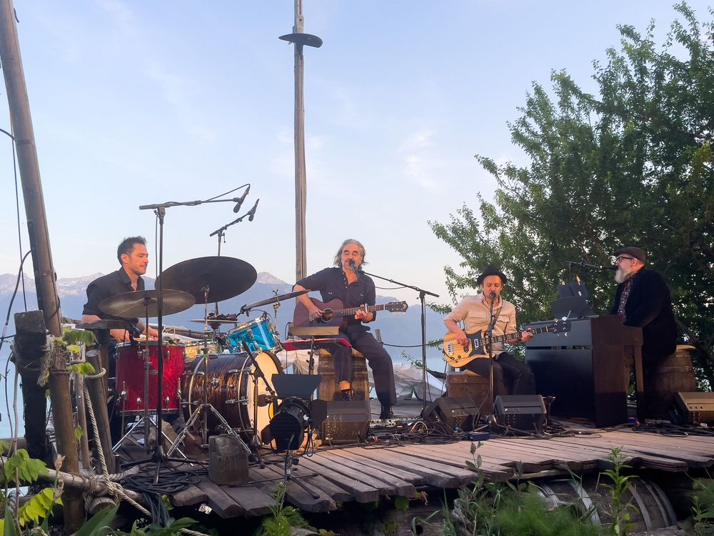 Musicians performing on an outdoor stage with instruments and equipment during a live concert.