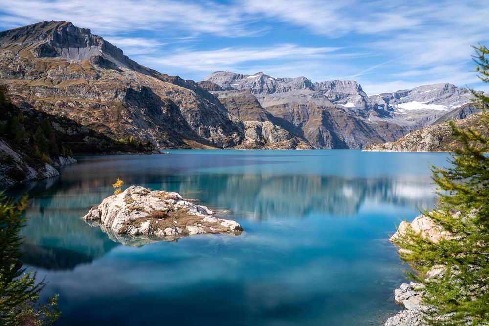 Turquoise alpine lake surrounded by rugged mountain peaks with a rocky island in the center.