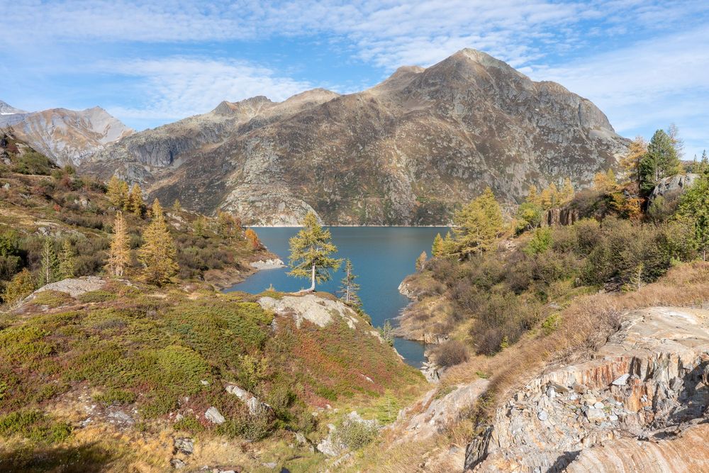 Panoramic mountain landscape with turquoise alpine lake surrounded by rugged peaks and autumn foliage.