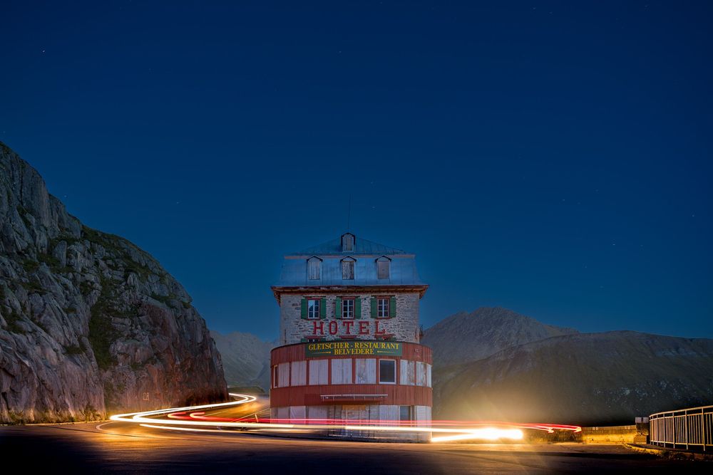Time lapse photograph captures light trails from passing vehicles against a dark sky with an illuminated building.