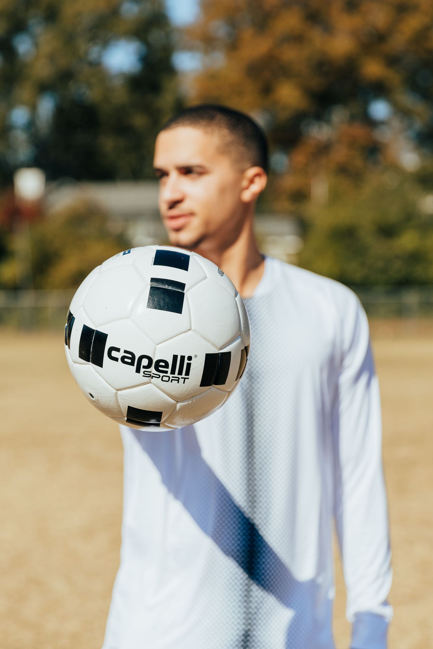 Male athlete in white Capelli Sport jersey extending a soccer ball toward the camera.