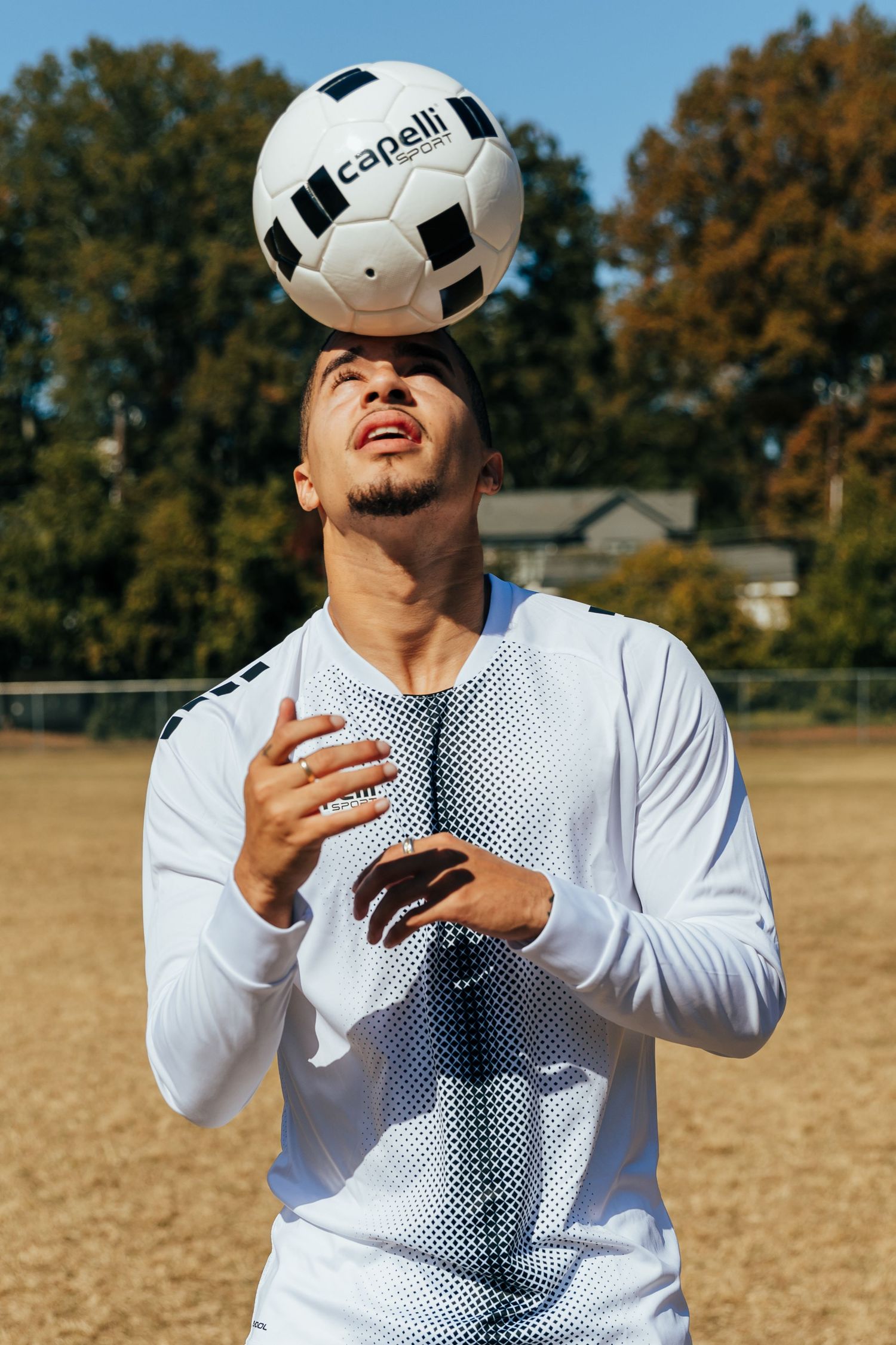 Male soccer player balancing a Capelli Sport ball on his head on an outdoor field.