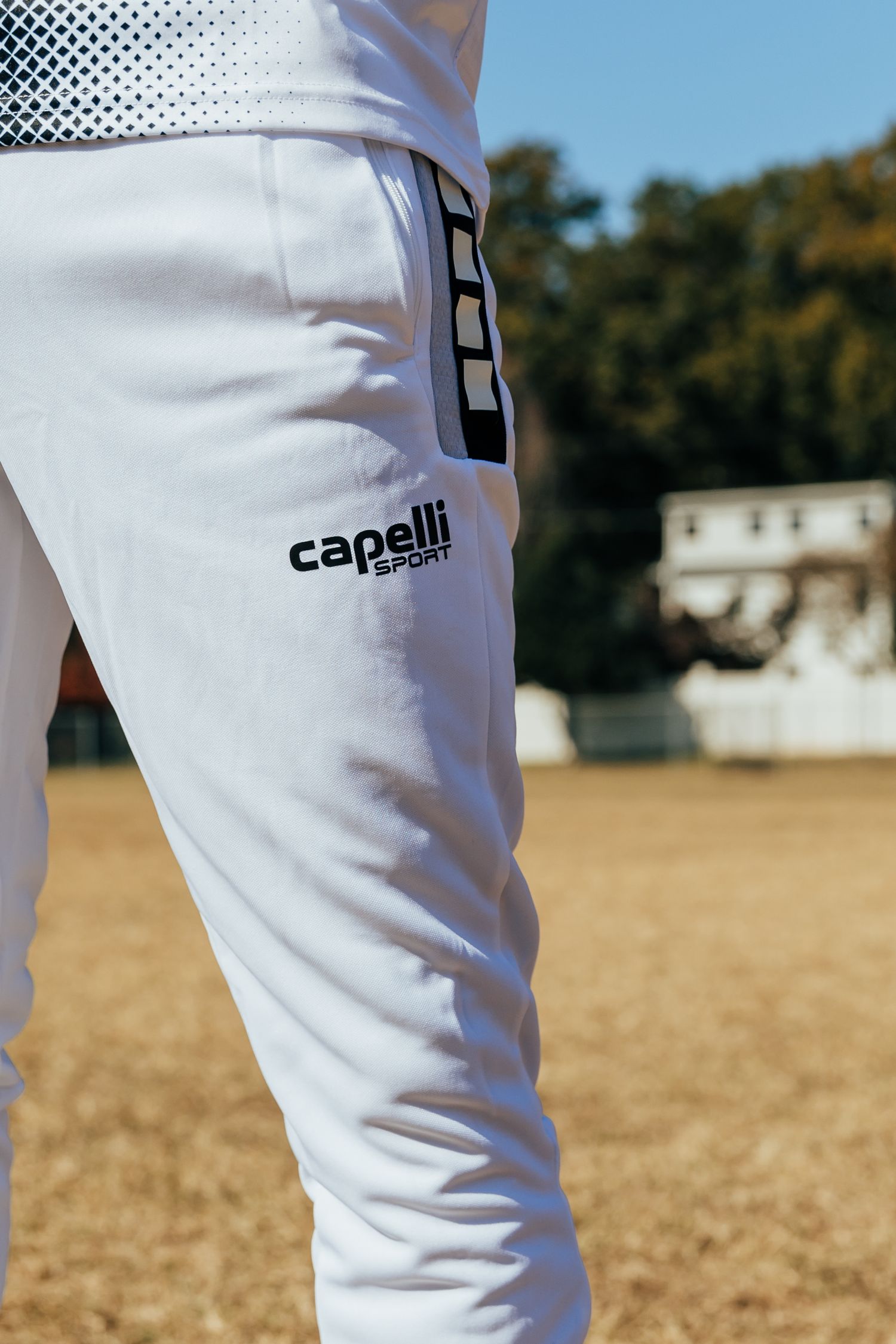 Close-up of white Capelli Sport jogger pants with logo on a male athlete outdoors.