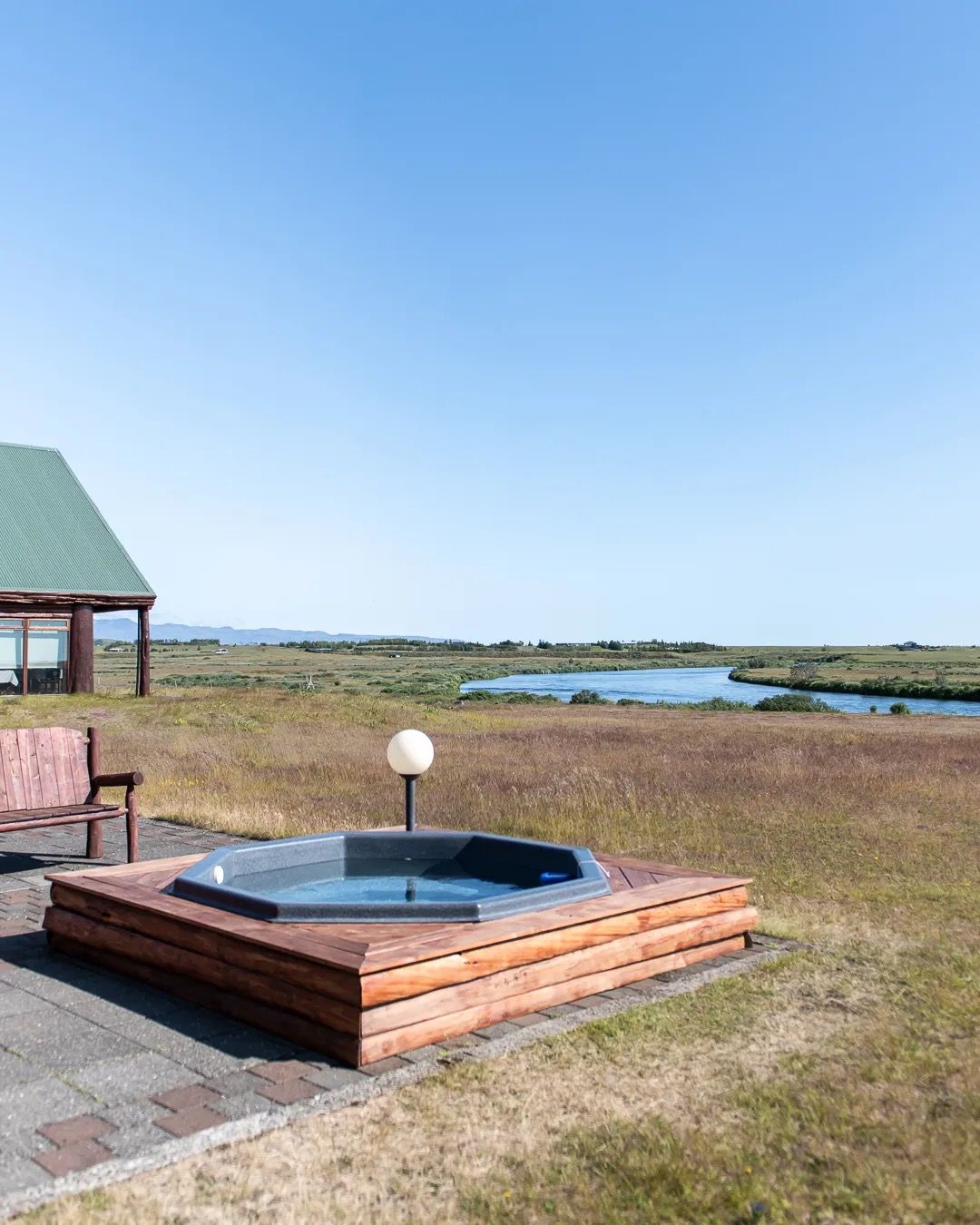 Outdoor wooden hot tub overlooking open fields and the coastline on a sunny day.