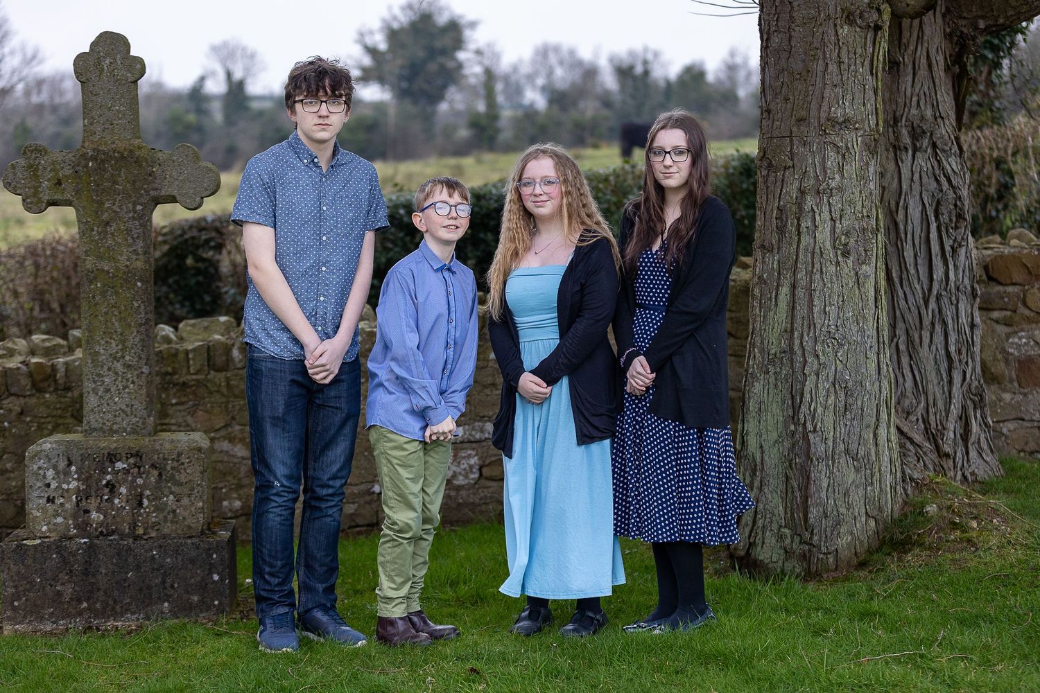 A group stands together in a casual outdoor setting near trees and stone structures.