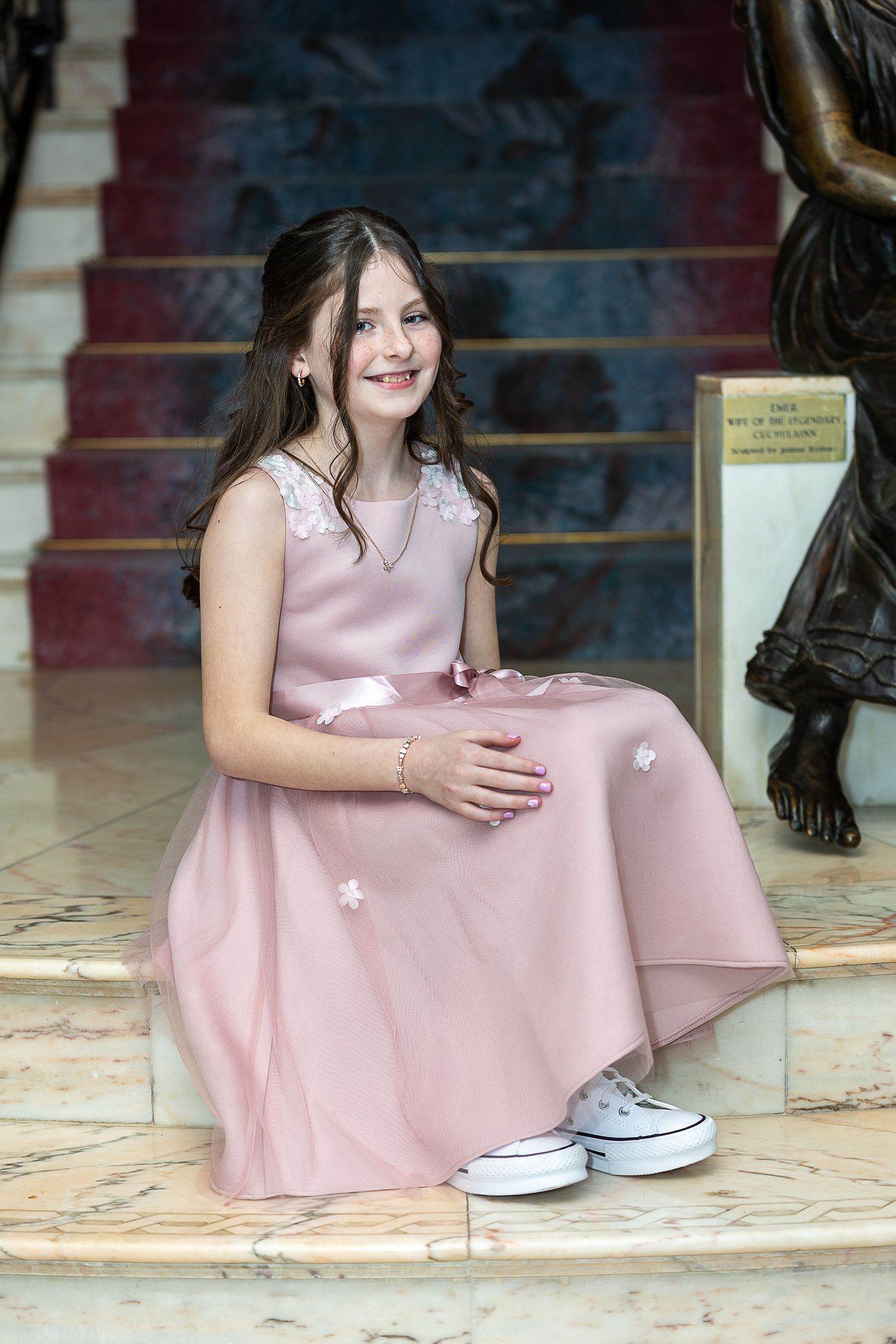 A young person in a pink dress and white sneakers sits on a marble floor in a series of candid poses.
