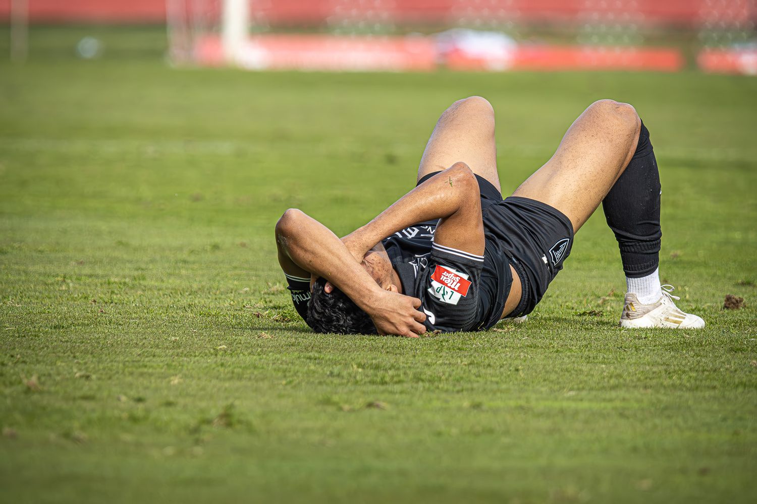 Soccer players lie on the grass field after an intense play during a competitive match.