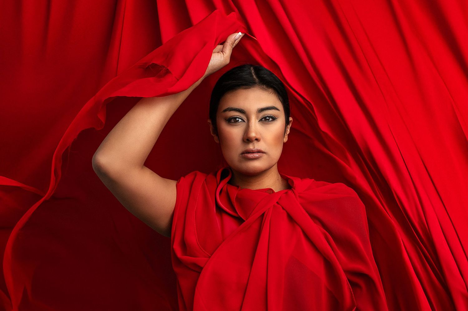 A figure in a flowing red dress poses dramatically against a bright red background creating a striking monochromatic scene.