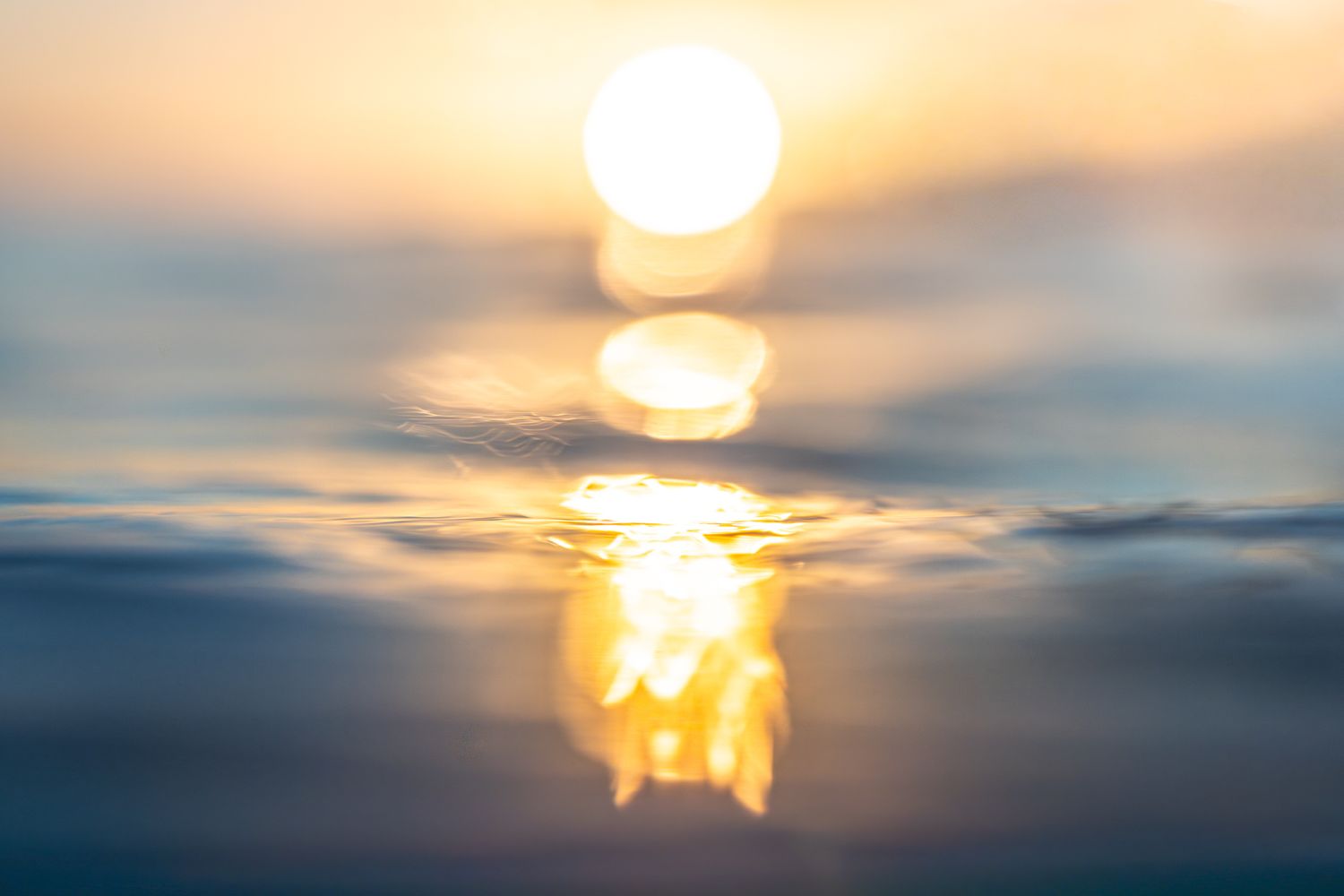 Underwater view looking up at sunlight filtering through rippling ocean surface creating ethereal blue-green illumination.