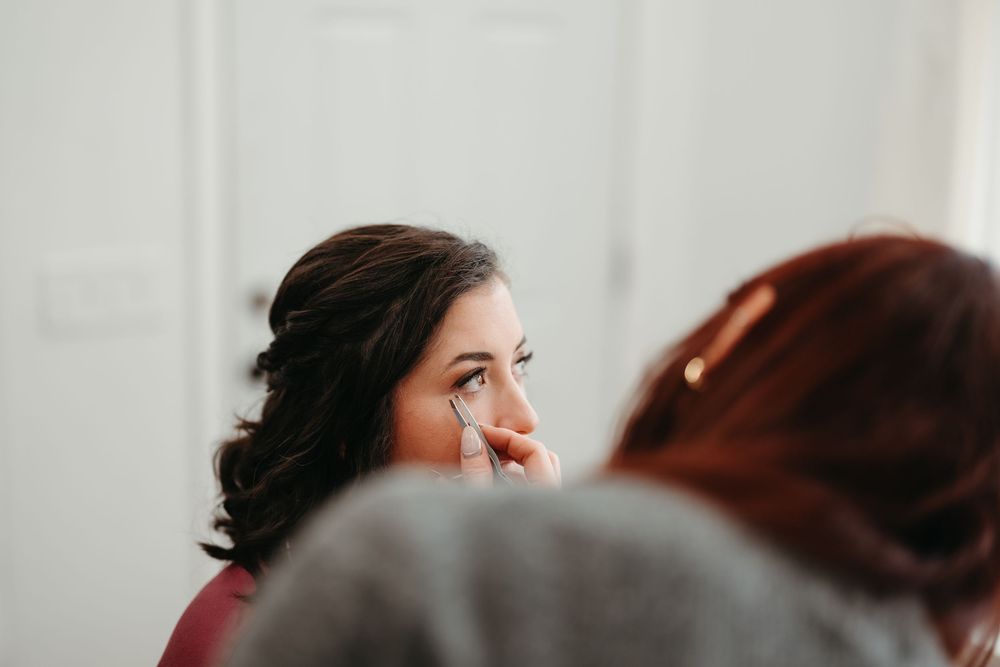 Two people share a candid moment during a makeup application session in a bright indoor space.