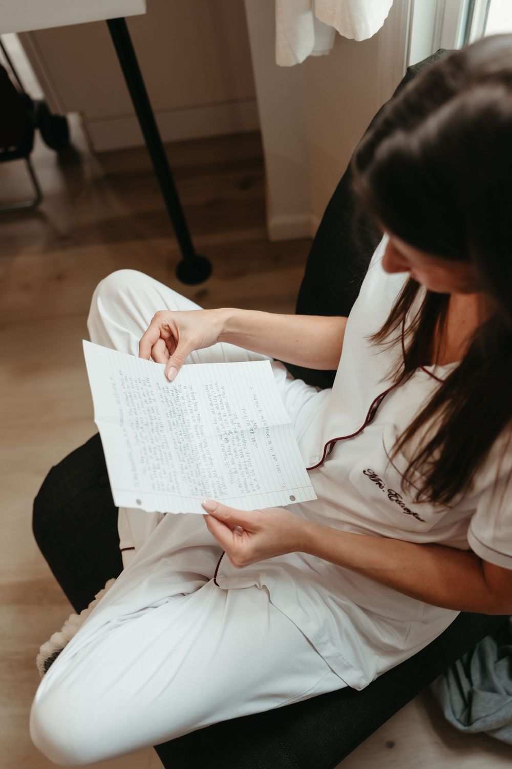 Person in white shirt sits on floor reviewing papers and documents in a casual indoor setting.