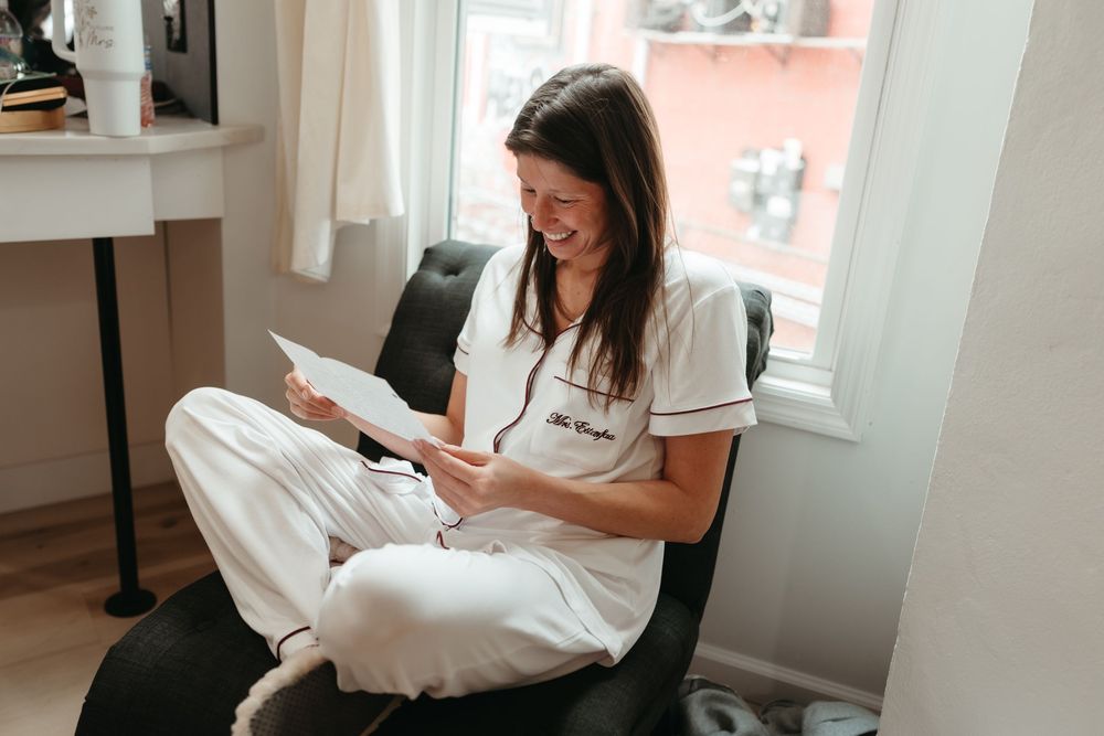 Healthcare professional in white scrubs sits comfortably in chair while reading documents near window.