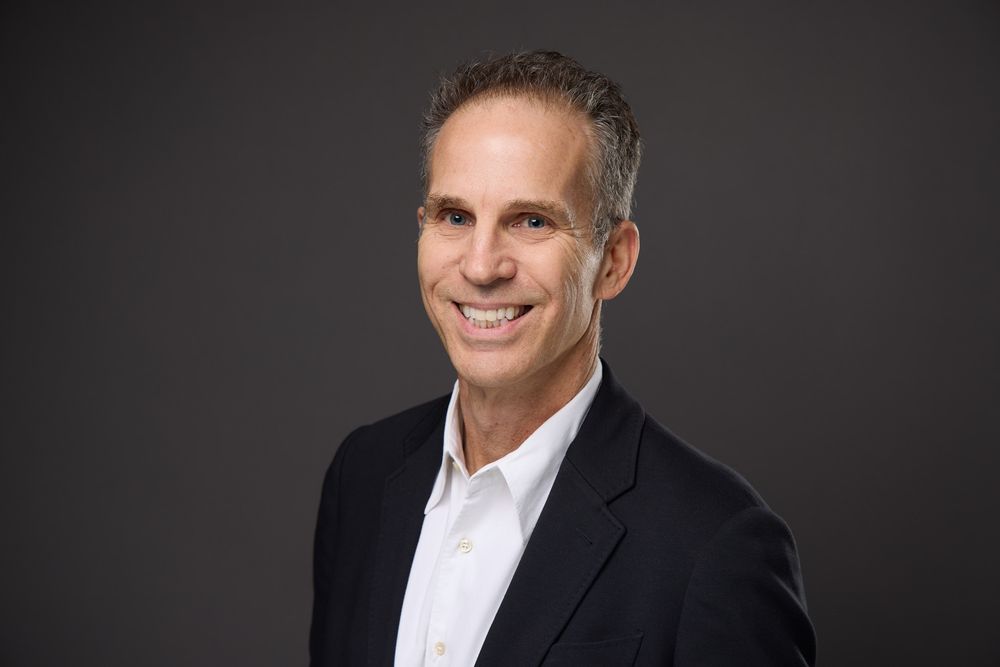 Professional headshot series showing a man in a black suit and white shirt against a dark background smiling at the camera.