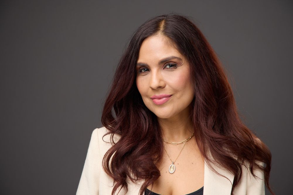 Professional headshot of a woman with dark hair and a black top against a dark gray background.
