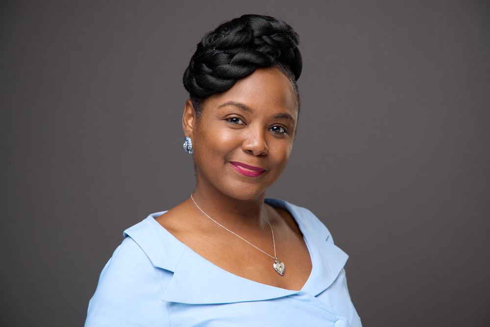 Professional studio portrait with light blue blouse against dark gray background.