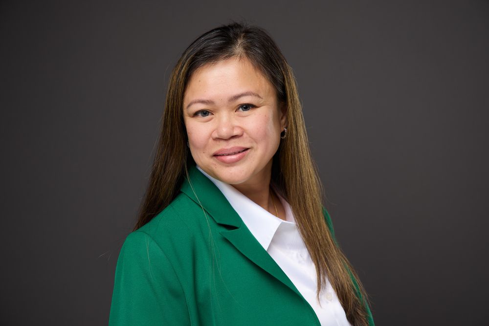 Professional headshot portrait of someone wearing a green blazer and white shirt against a dark background.