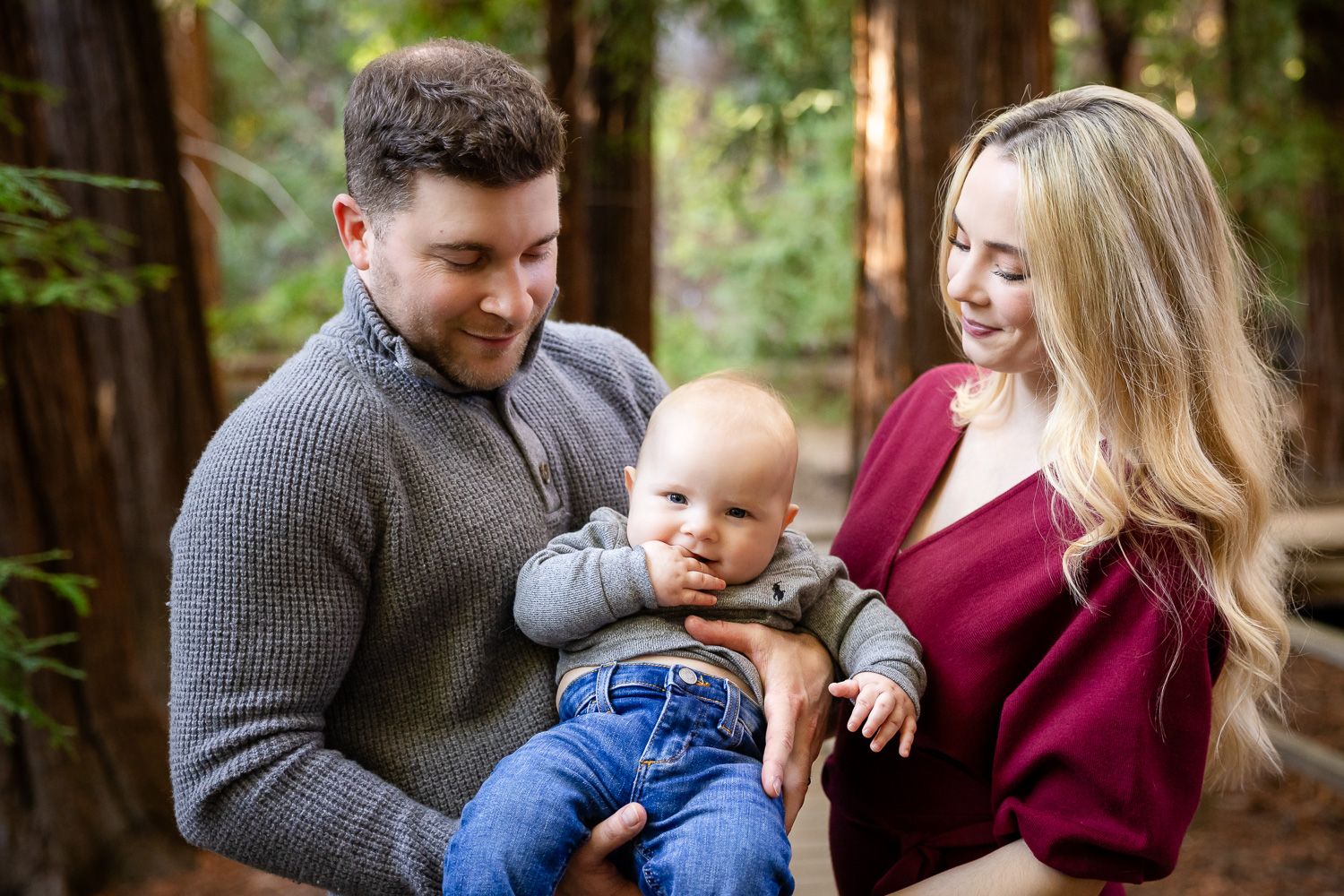 A family shares joyful moments together in a redwood forest setting wearing coordinated burgundy and gray outfits.