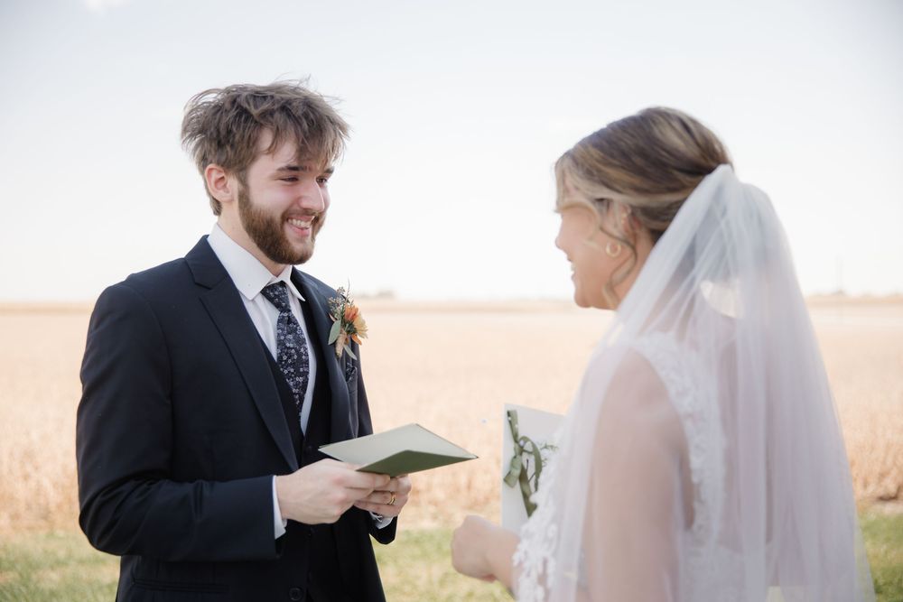 A couple exchanges vows during an outdoor wedding ceremony at sunset in a golden field.