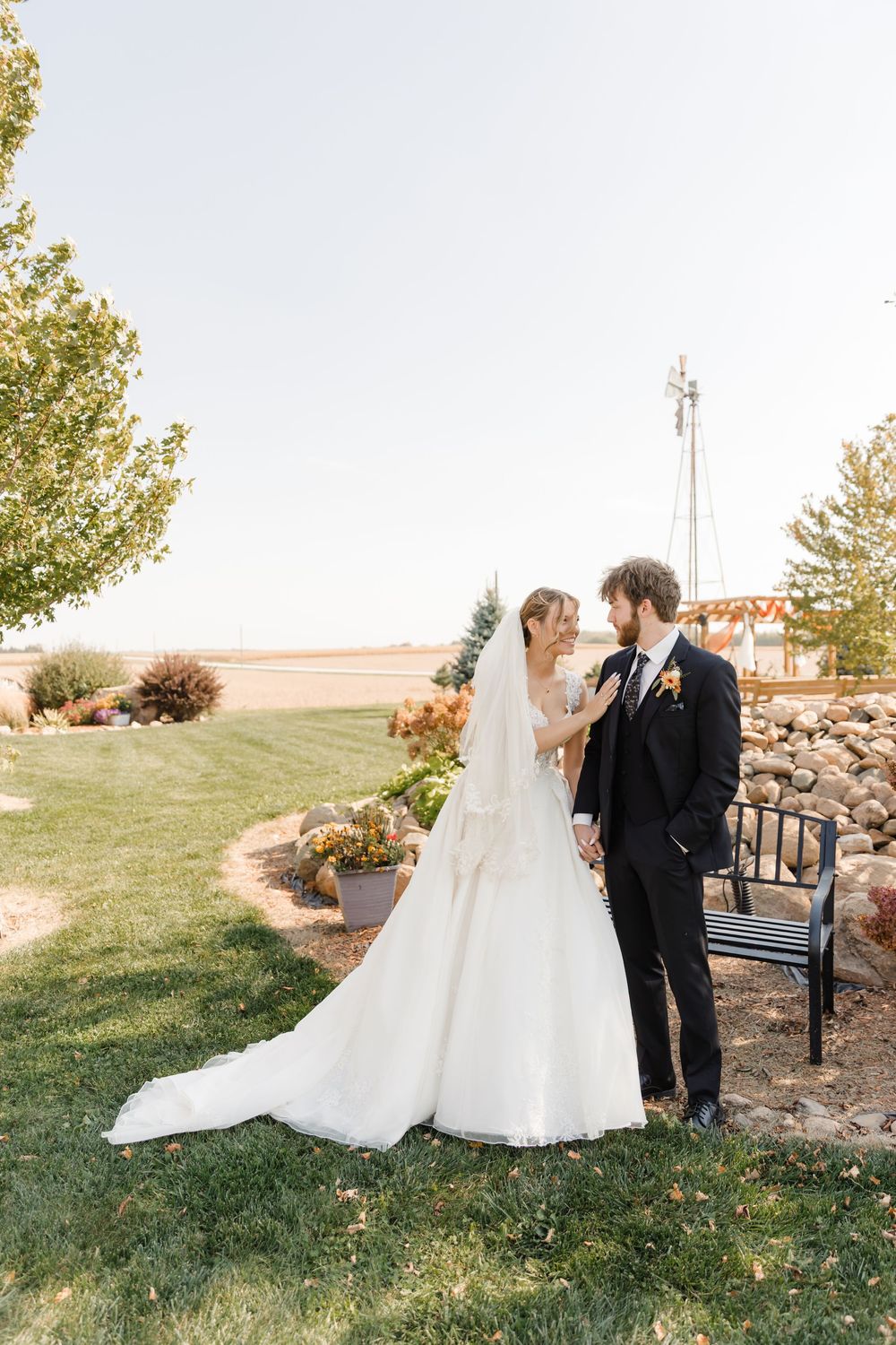 Romantic outdoor wedding couple embraces on a grassy hillside with a flowing white dress and black suit.