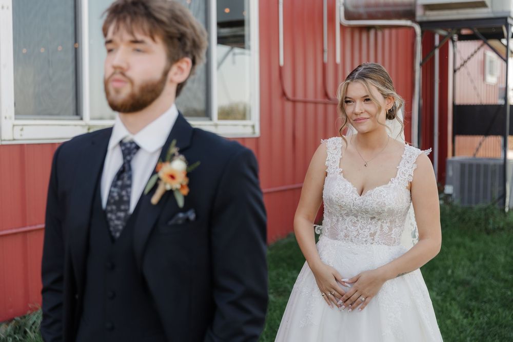 A wedding couple poses outdoors in front of a rustic red barn on their special day.