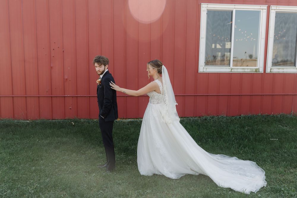 A wedding couple shares a playful moment outside a red barn on their special day.