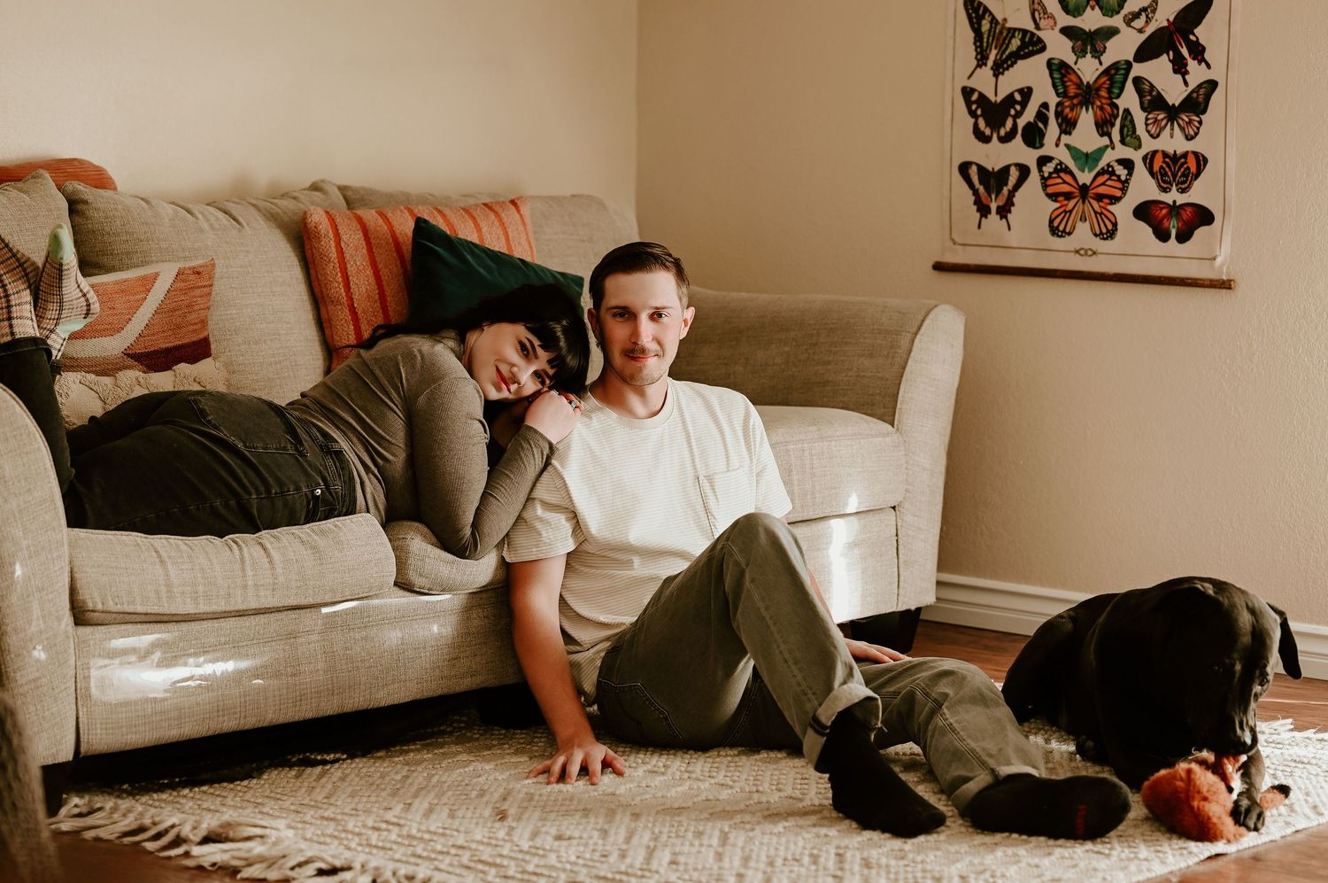 A person lounges on a couch with a black and brown dog in a cozy living room setting.