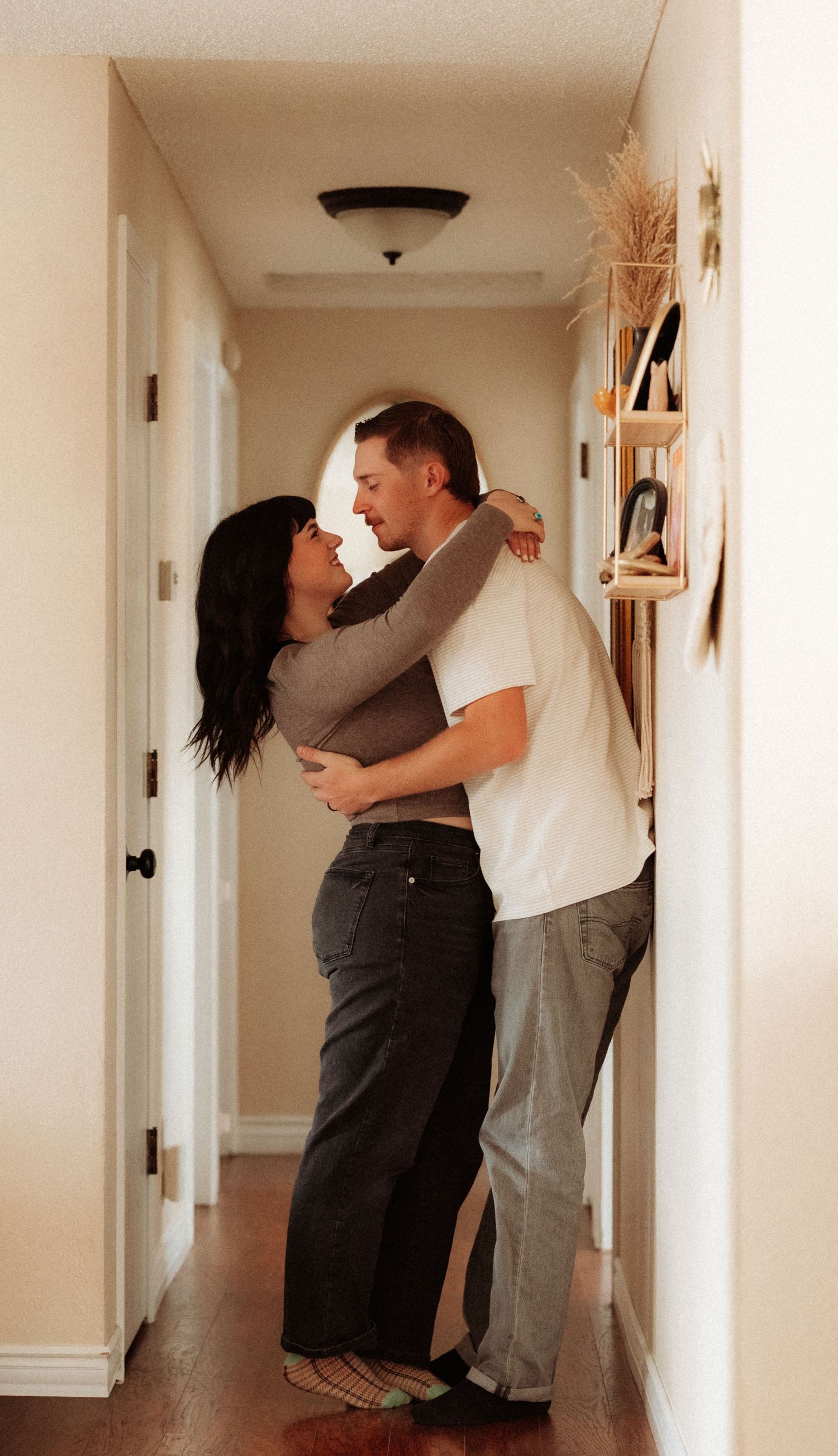 A couple embraces lovingly in a warm-lit hallway of their home.