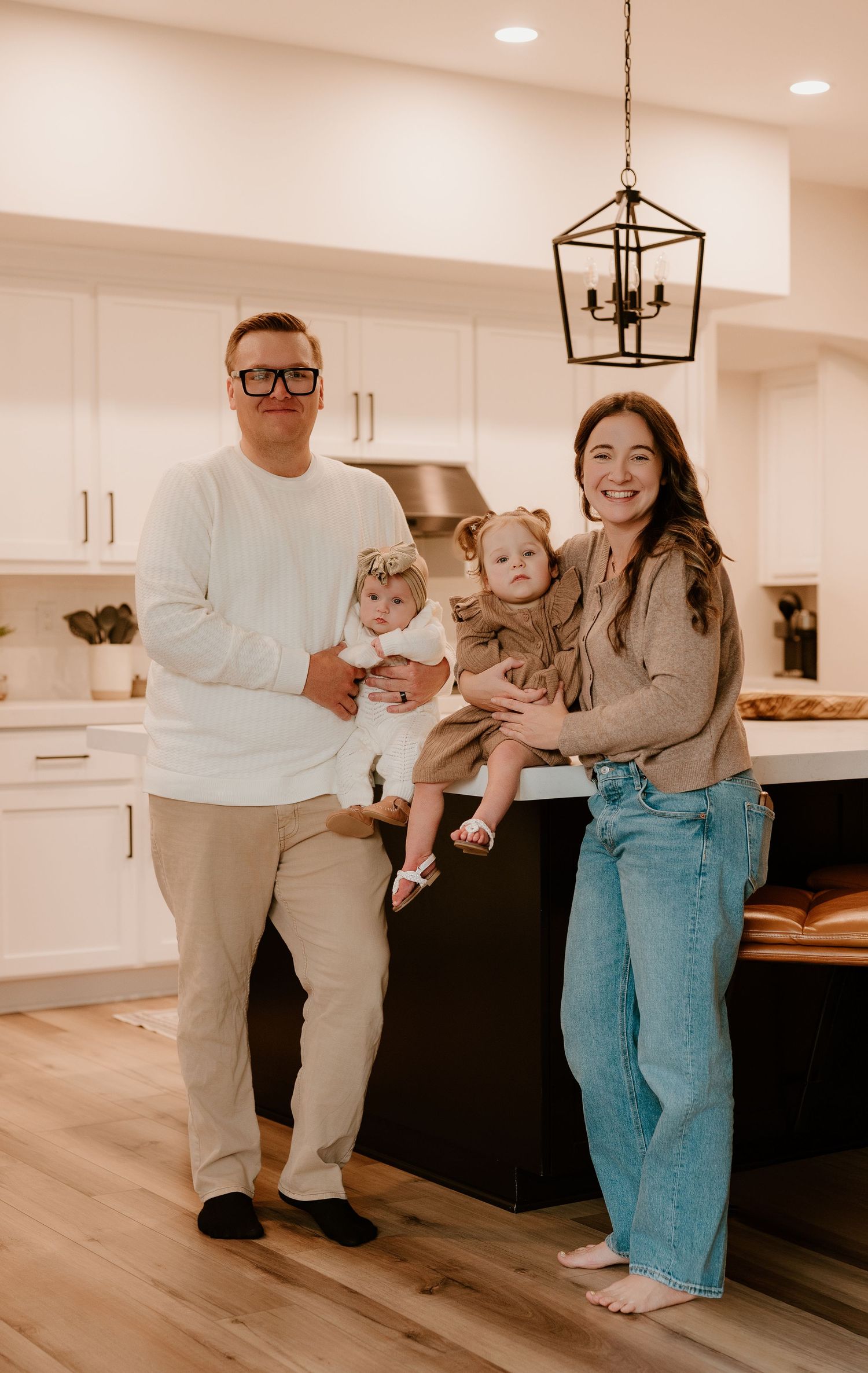 Family poses together in modern living room with white cabinets and hardwood floors in warm lighting.