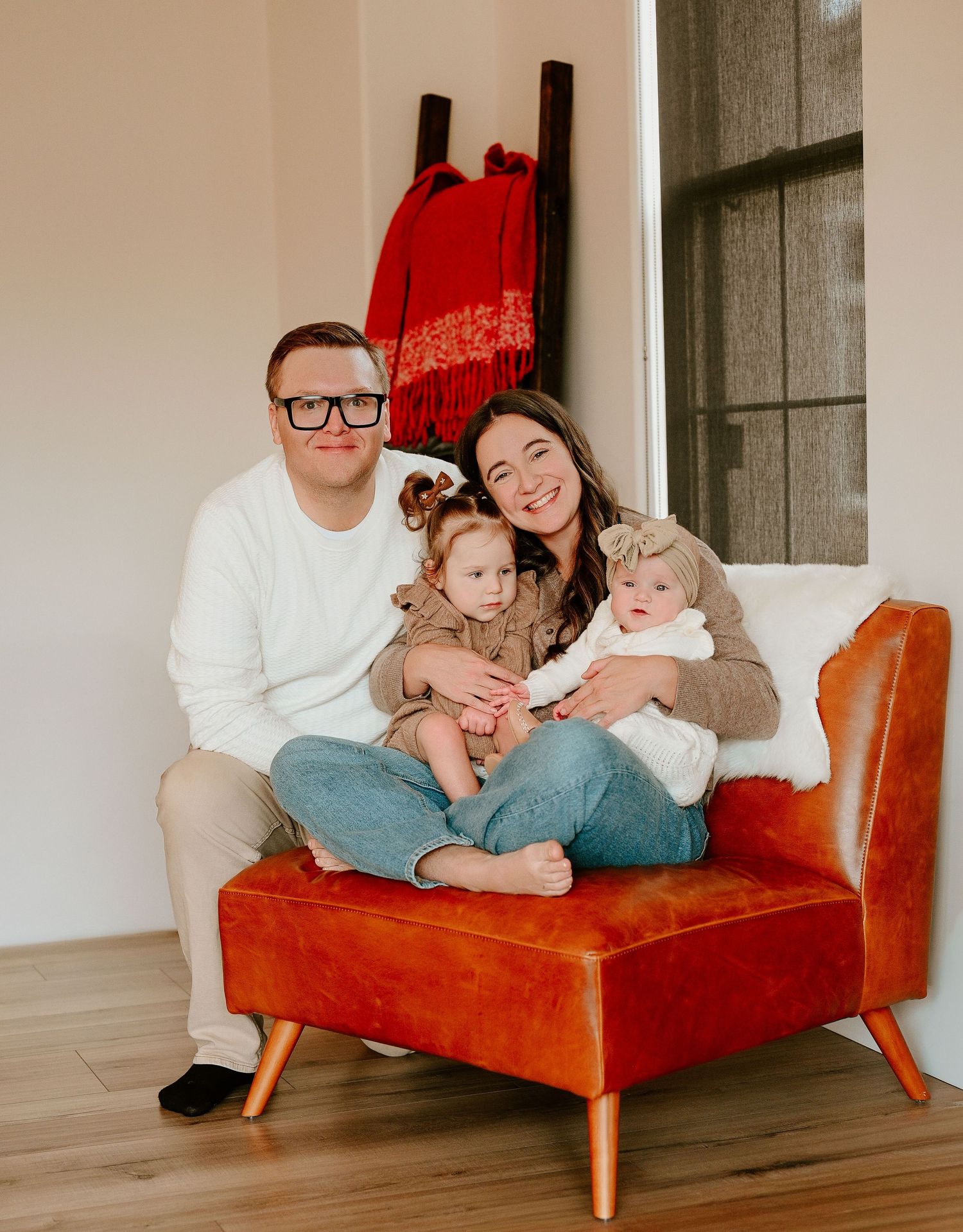 A family sits together on a red mid-century modern daybed in a minimalist white room.