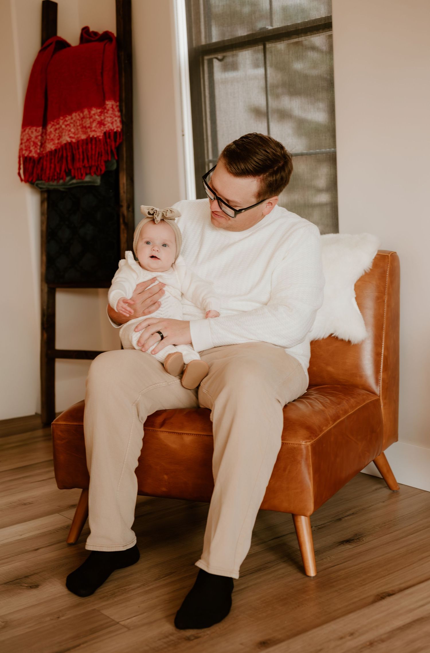 A series of four photos showing a baby sitting on a brown leather chair in a minimalist interior setting.