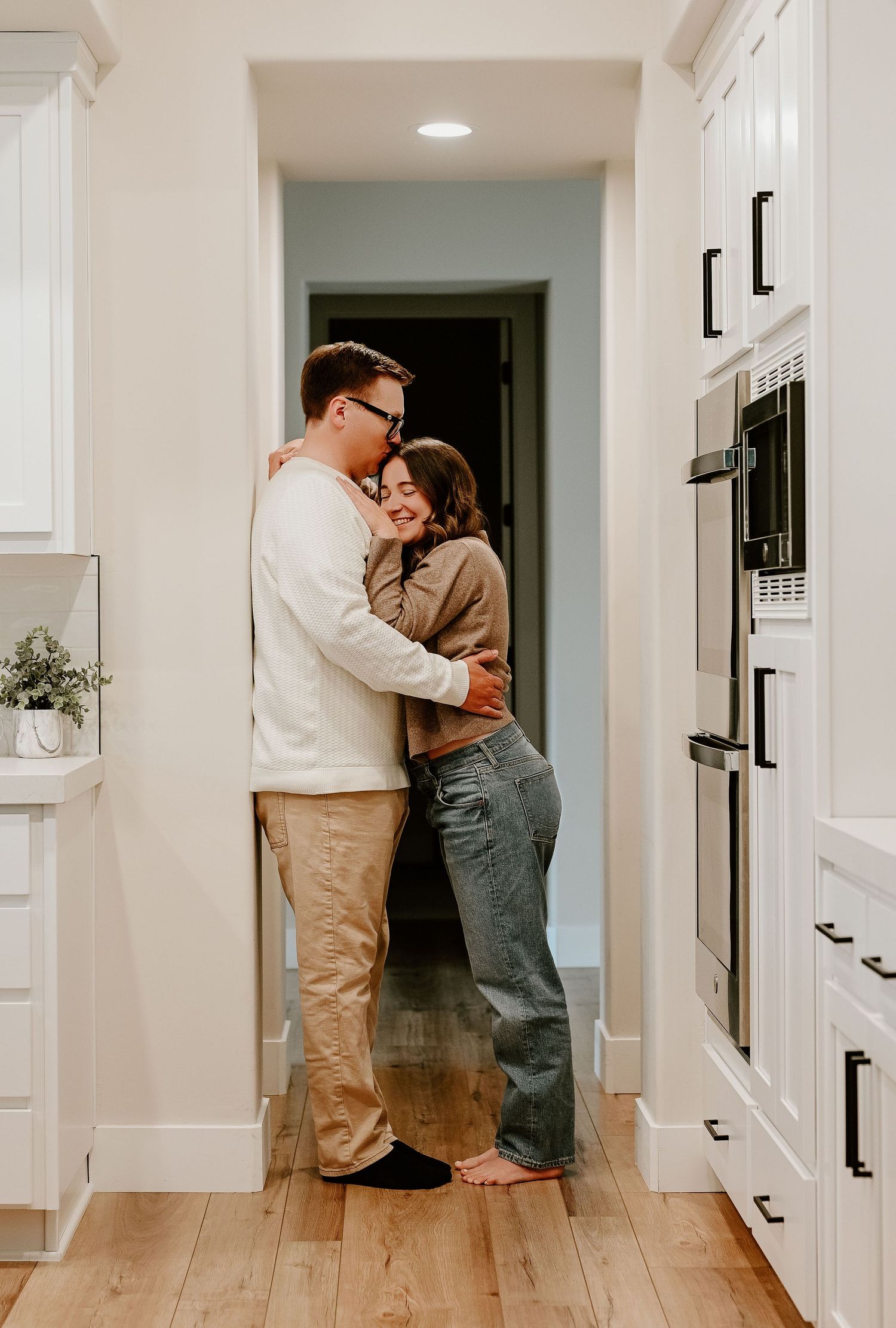 A series of tender romantic moments captured in a bright modern hallway with white walls and light hardwood floors.