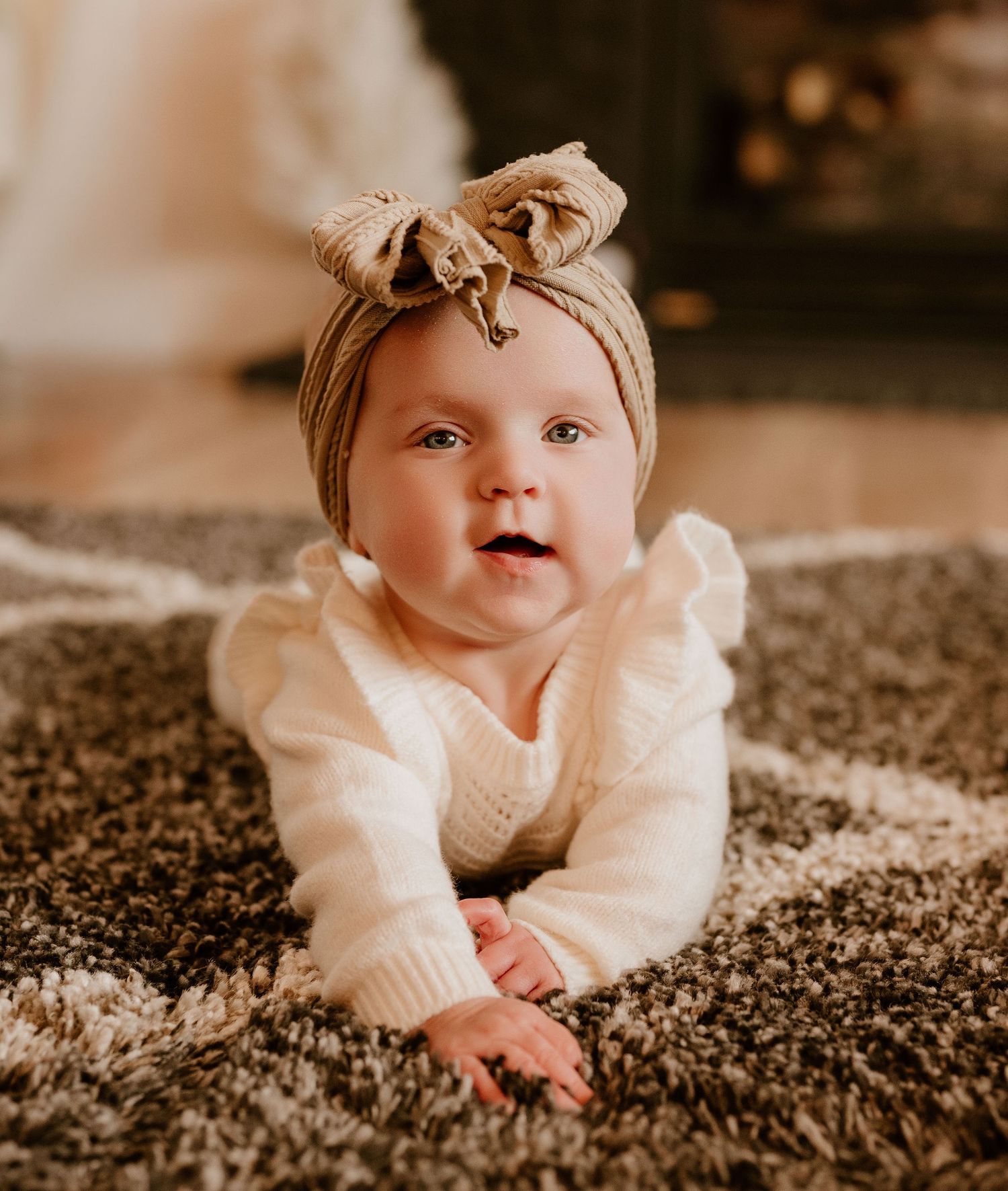 A baby in cream-colored knit clothing lies on a plush carpet in a warm-toned sepia photograph.